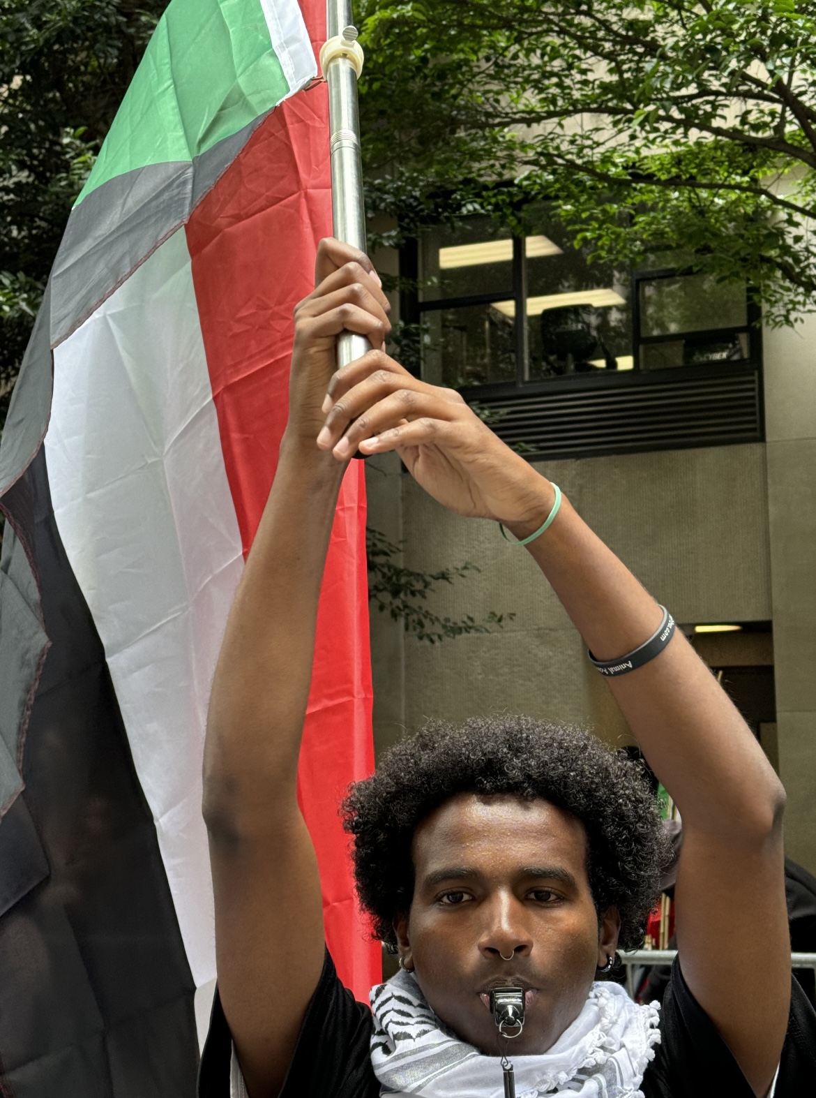 Image of a man holding a flag and blowing a whistle at a protest.