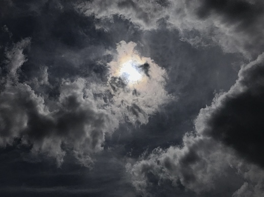 Dramatic sky with dark clouds partially covering the sun.