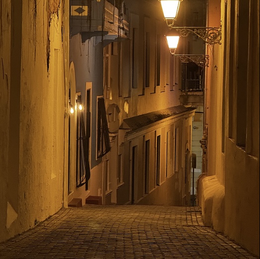 Narrow cobblestone alleyway in San Juan at night illuminated by warm street lamps.