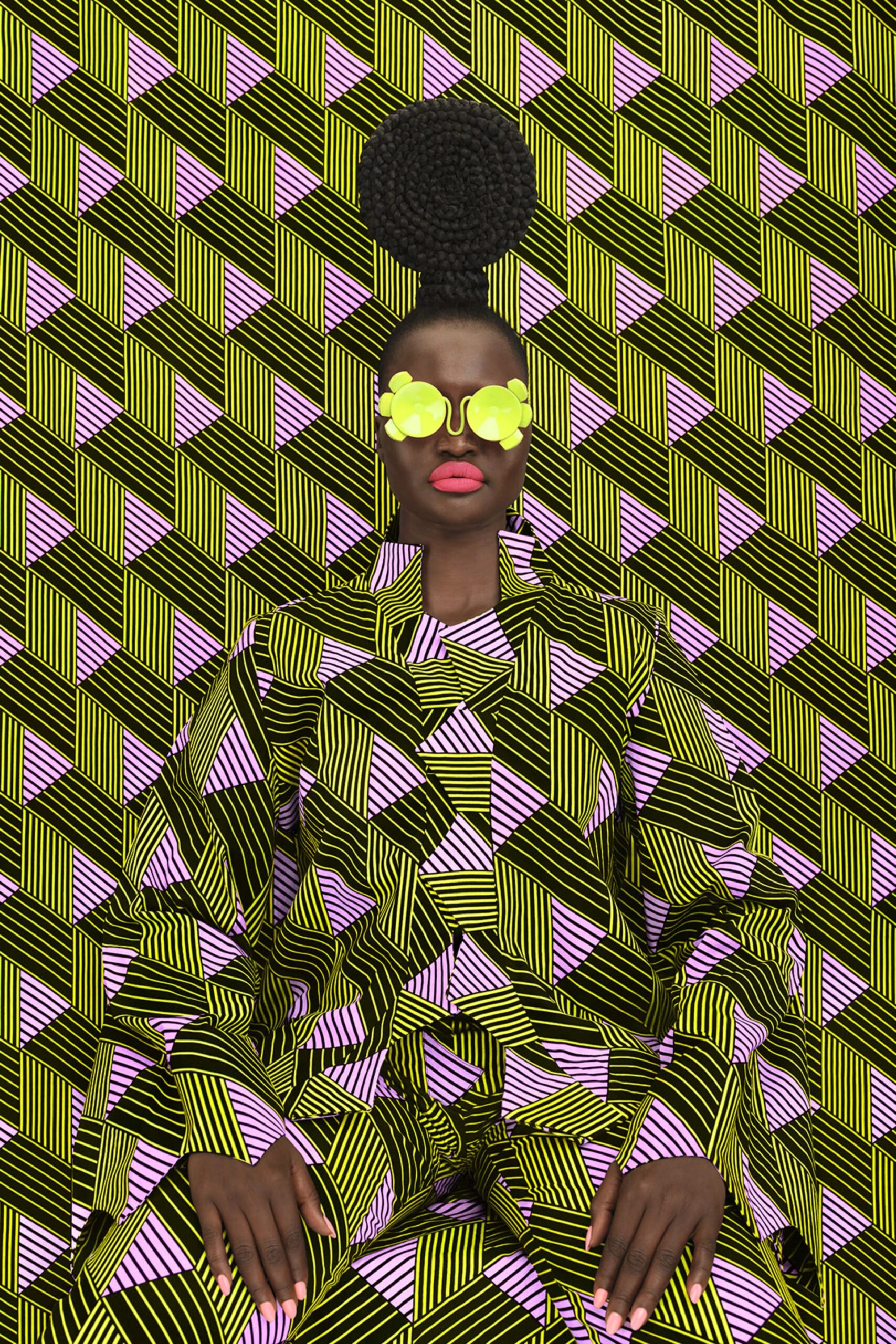 Photo of an African-American woman in a geometric-patterned outfit blending into a matching background, wearing sunglasses and a braided hair crown