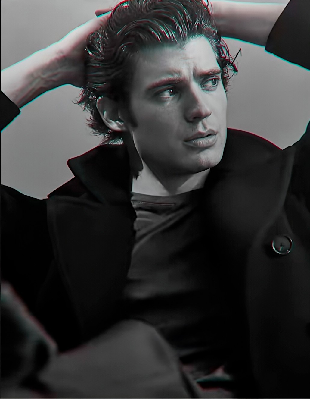 photographic black and white portrait of a young man looking away from the camera with his hands folded behind his head