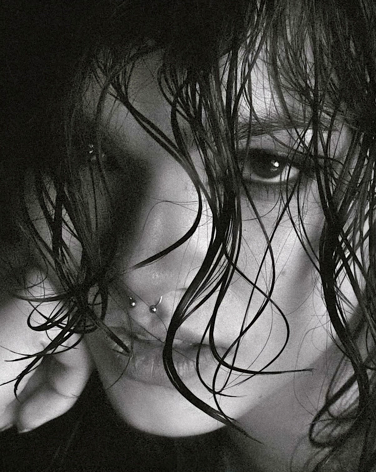 A black and white close-up photograph of a young woman's face with wet hair partially covering their face.