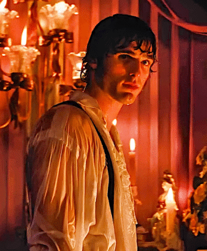 color photograph of a young handsome caucasian man wearing a white ruffled shirt that looks wet in a candle lit room
