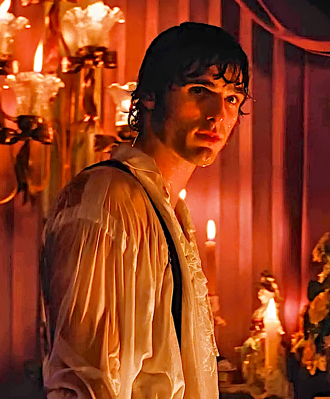 color photograph of a young handsome caucasian man wearing a white ruffled shirt that looks wet in a candle lit room