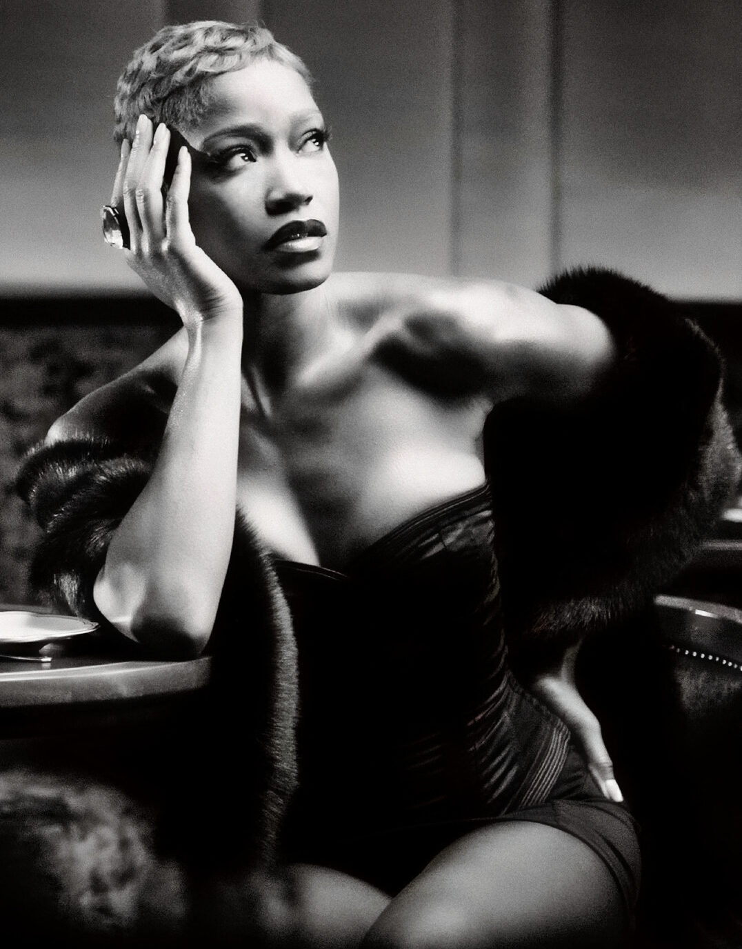 Black and white photograph of Keke Palmer seated at a table holding her head with her right hand looking away from the camera