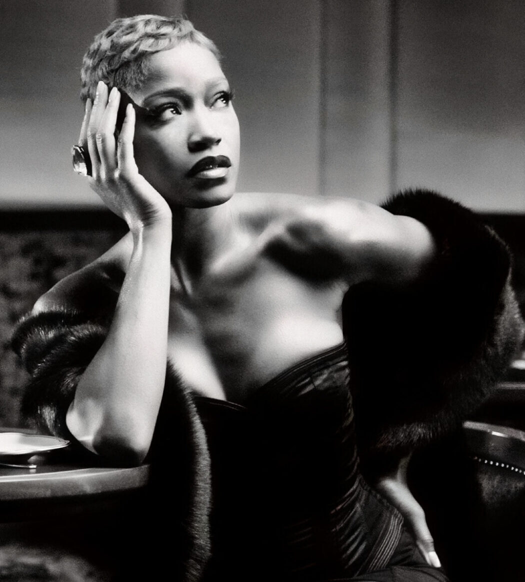 Black and white photograph of Keke Palmer seated at a table holding her head with her right hand looking away from the camera